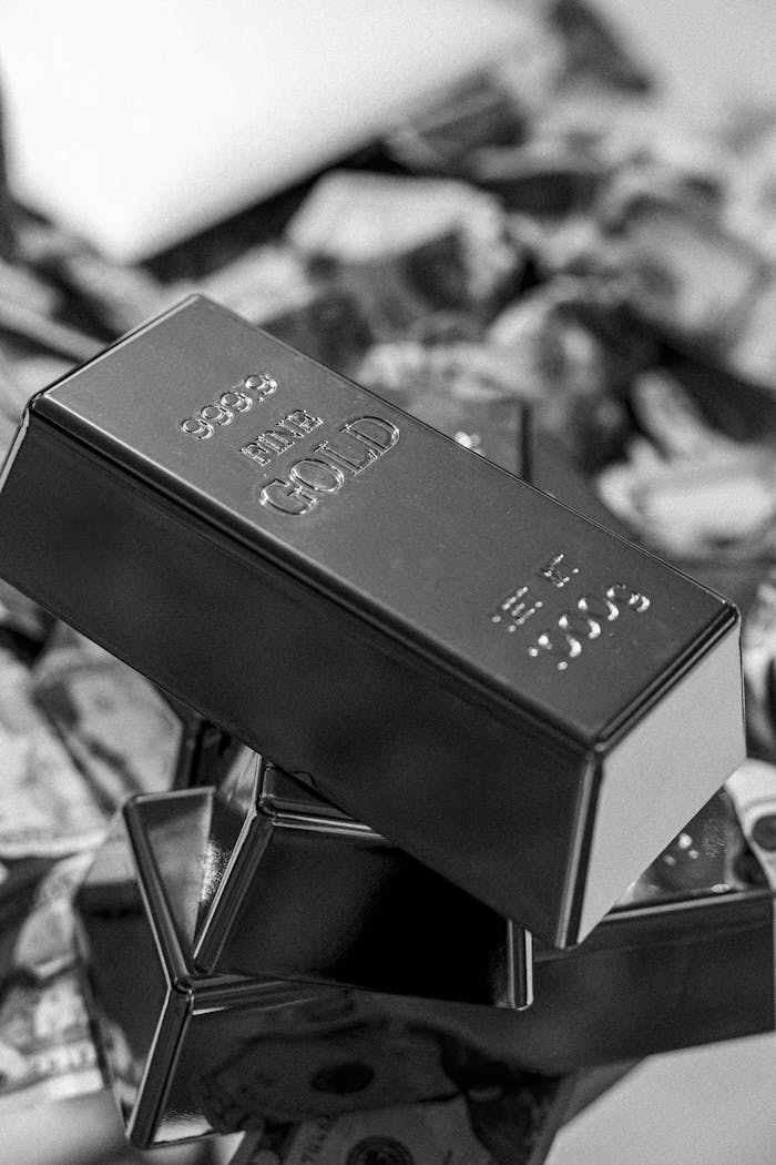 Fine gold bars stacked on currency in monochrome, symbolizing wealth and investment.